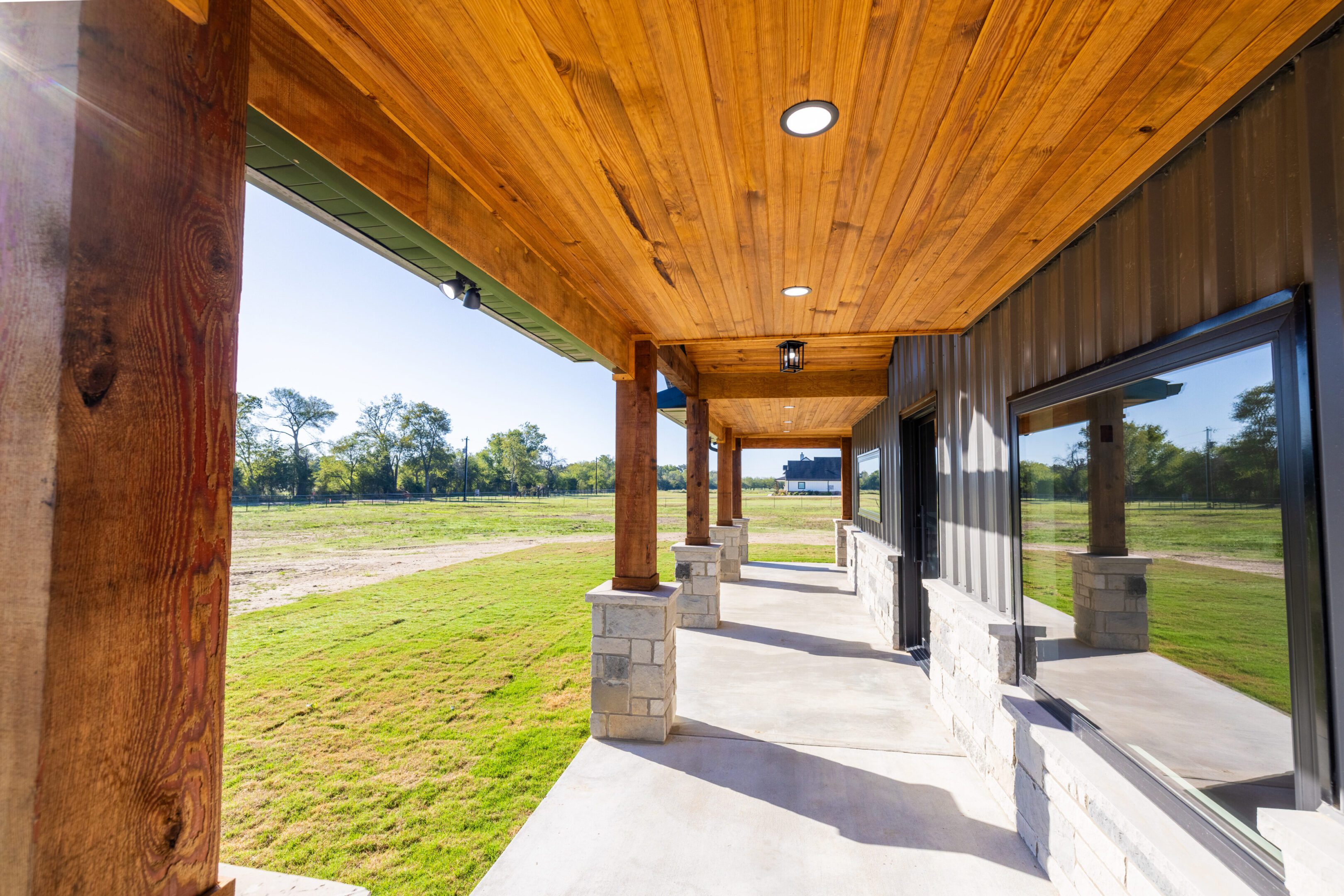 A porch with wood ceilings and pillars in the middle of an open field.